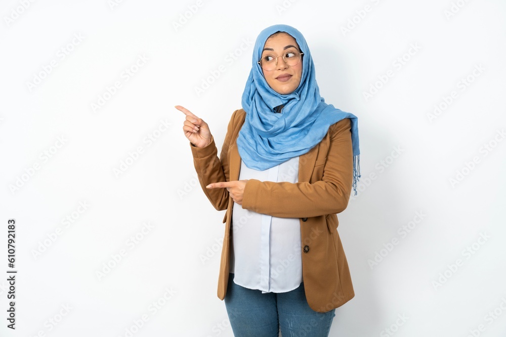 Optimistic Young beautiful pregnant muslim woman wearing hijab over white background points with both hands and looking at empty space. Optimistic Young beautiful pregnant muslim woman wearing hijab over white background points with both hands and looking at empty space.