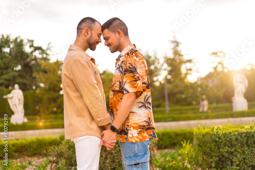 Romantic portrait of gay couple looking at each other at sunset in a park in the city. Diversity and lgbt concept © unai