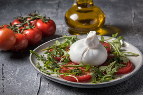 Burrata cheese with tomatoes, arugula and pesto sauce on a marble table.