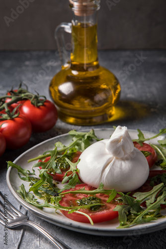 Burrata cheese with tomatoes, arugula and pesto sauce on a marble table.