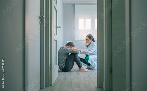 Female doctor reassuring and helping with empathy to male patient sitting on the room floor of a mental health center