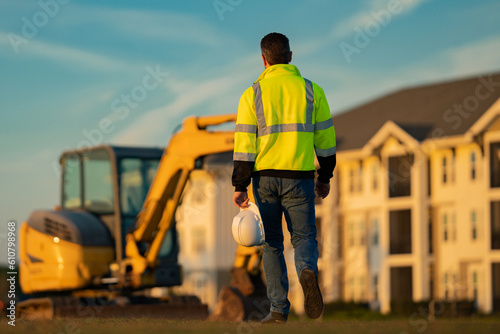 Construction build man with excavator at industrial site. Worker in helmet with bulldozer. Engineer work with builder contractor in hardhat. Excavation foreman with tractor. Workman with excavator.