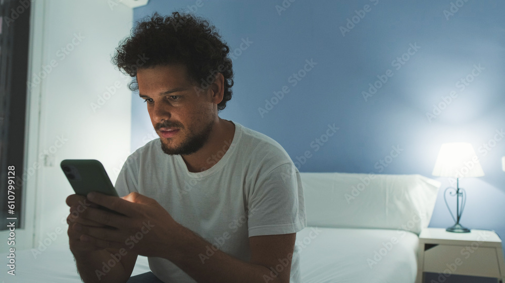 Guy is sitting on the bed in the bedroom, watching video, movie on mobile phone Guy is sitting on the bed in the bedroom, watching video, movie on mobile phone