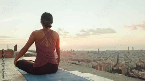 Young woman in bodysuit practices yoga at sunrise at viewpoint. Back view © Andrii Nekrasov