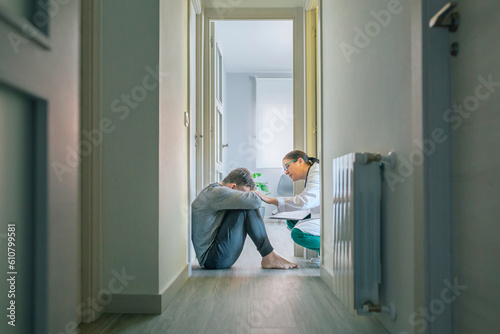 Female doctor reassuring and helping with empathy to male patient sitting on the room floor of hallway