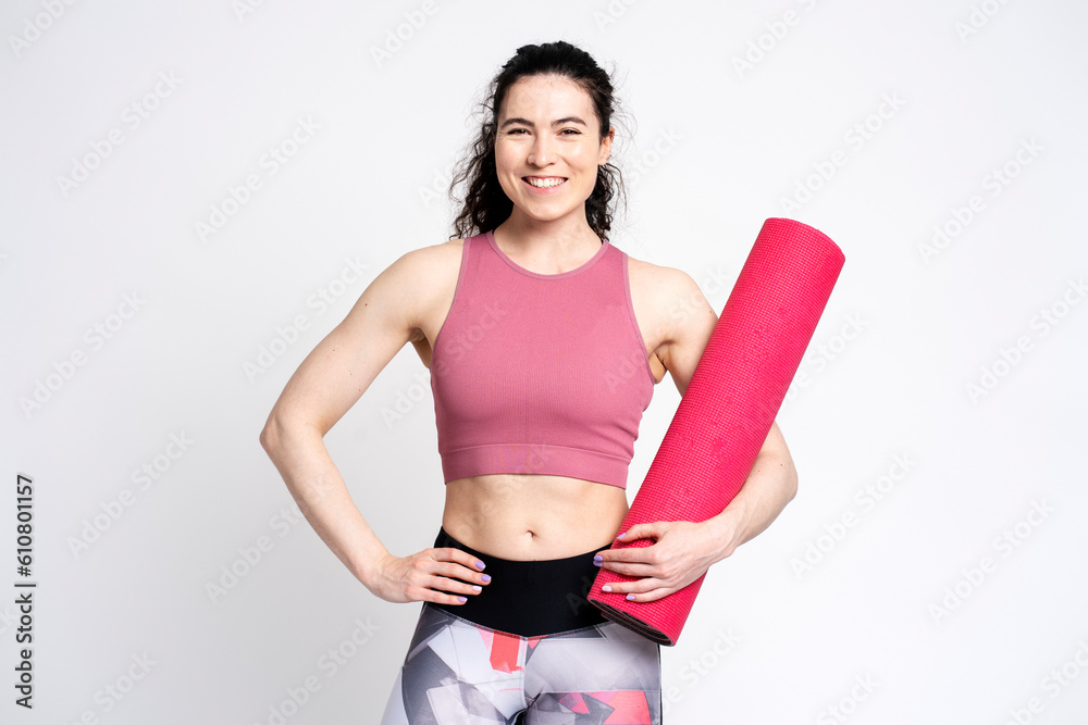 Confident young fit woman smiling looking at camera carrying fitness yoga mat