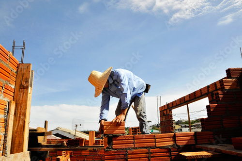 pedreiro construtor edificando parede de tijolos em obra  photo