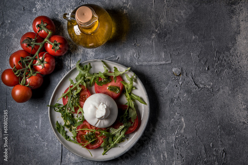 Burrata cheese with tomatoes, arugula and pesto sauce on a marble table.