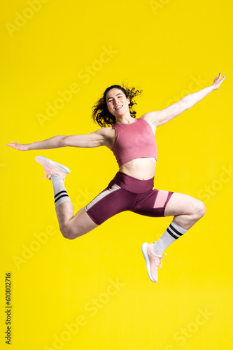Vertical studio portrait of a successful sportswoman jumping high up, looking at camera