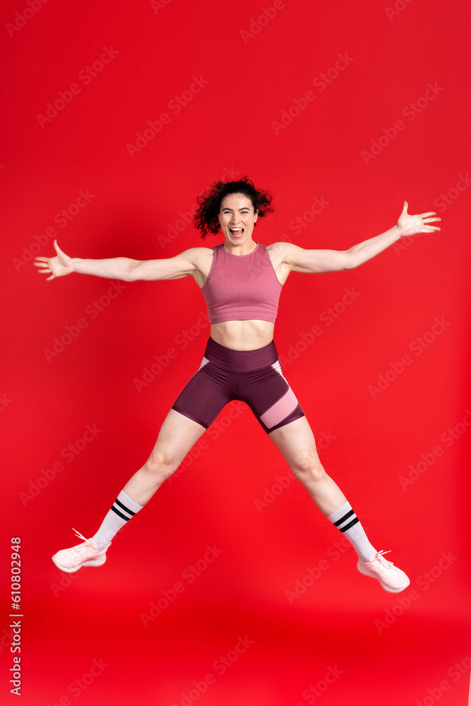 Young sportswoman looking at camera, performing stretching exercises and jumping high