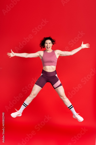 Young sportswoman looking at camera  performing stretching exercises and jumping high