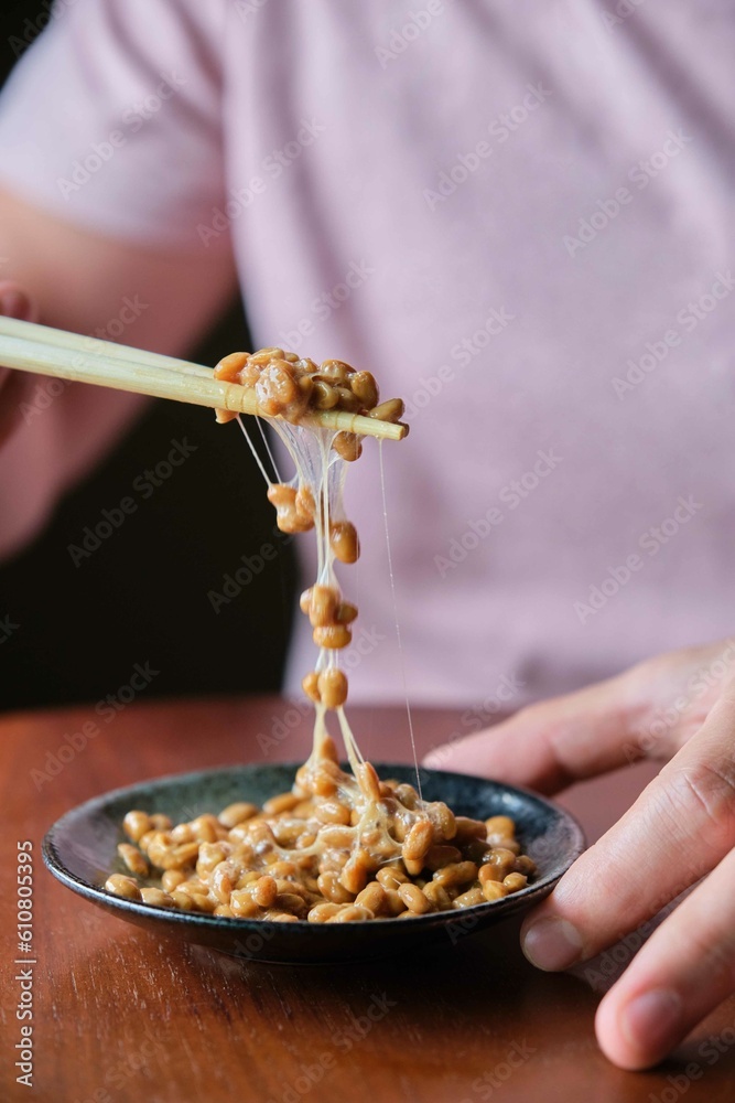 Unrecognizable man eating natto fermented soy beans with chopsticks.