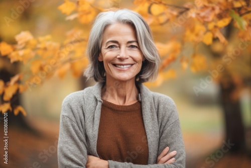 Portrait of a smiling senior woman standing with arms crossed in autumn park