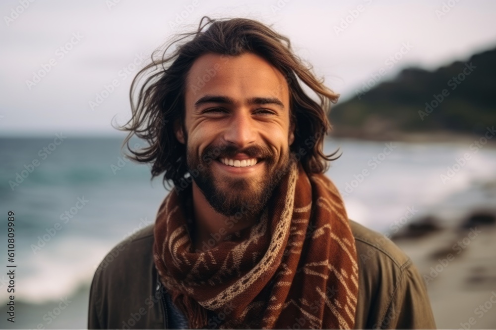 Portrait of a handsome young man smiling at the beach while wearing a scarf Portrait of a handsome young man smiling at the beach while wearing a scarf