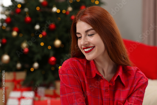 Beautiful young woman near Christmas tree indoors, space for text
