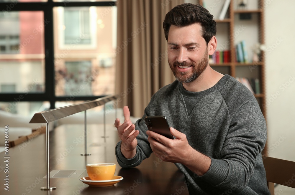 Handsome man sending message via smartphone at table indoors Handsome man sending message via smartphone at table indoors