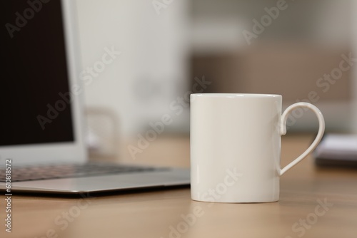 White ceramic mug and laptop on wooden table at workplace. Space for text