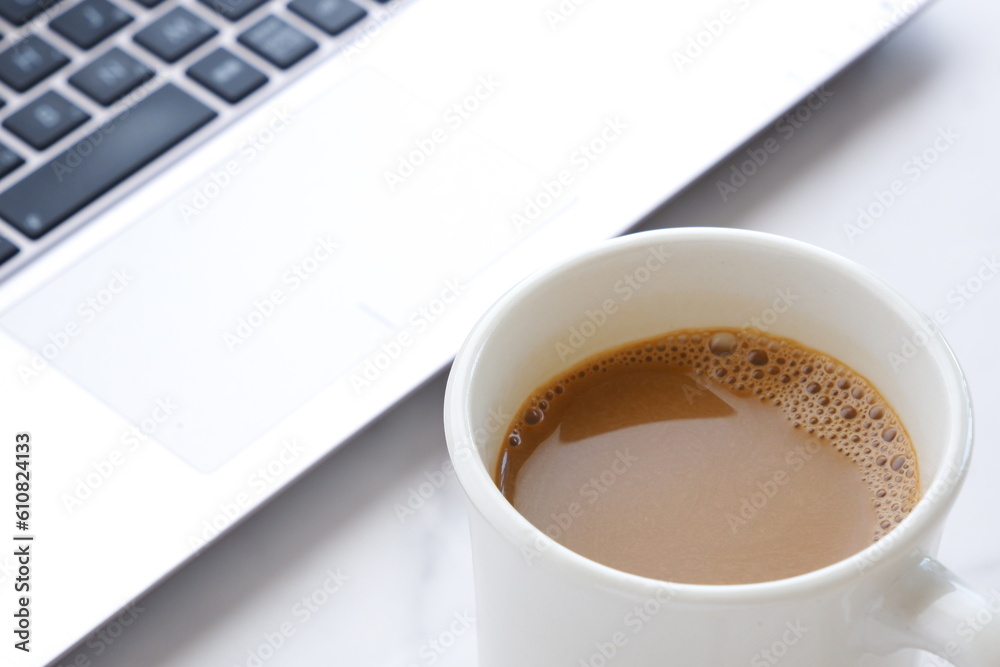 コーヒーを飲みながらノートパソコンでデスクワーク中のイメージ コーヒーを飲みながらノートパソコンでデスクワーク中のイメージ