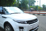 front view of white crossover car parked beside of tennis court. suv car with and green trees