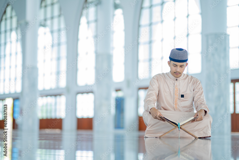 An Asian Muslim man is sitting and reading the Quran. The peace in the mosque makes it an energetic atmosphere of faith, with copy space, Arabic word translation: The Holy Al Quran. An Asian Muslim man is sitting and reading the Quran. The peace in the mosque makes it an energetic atmosphere of faith, with copy space, Arabic word translation: The Holy Al Quran.