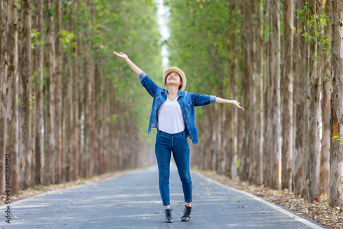 Asian tourist woman is jumping and dancing while having vacation at the national park while walking on the road with column of tree for travel and adventure