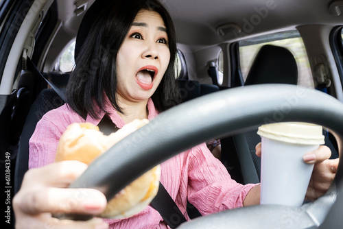 dangers of distracted eating while driving concept with careless Asian woman's car accident with food and drink in hand on steering wheel