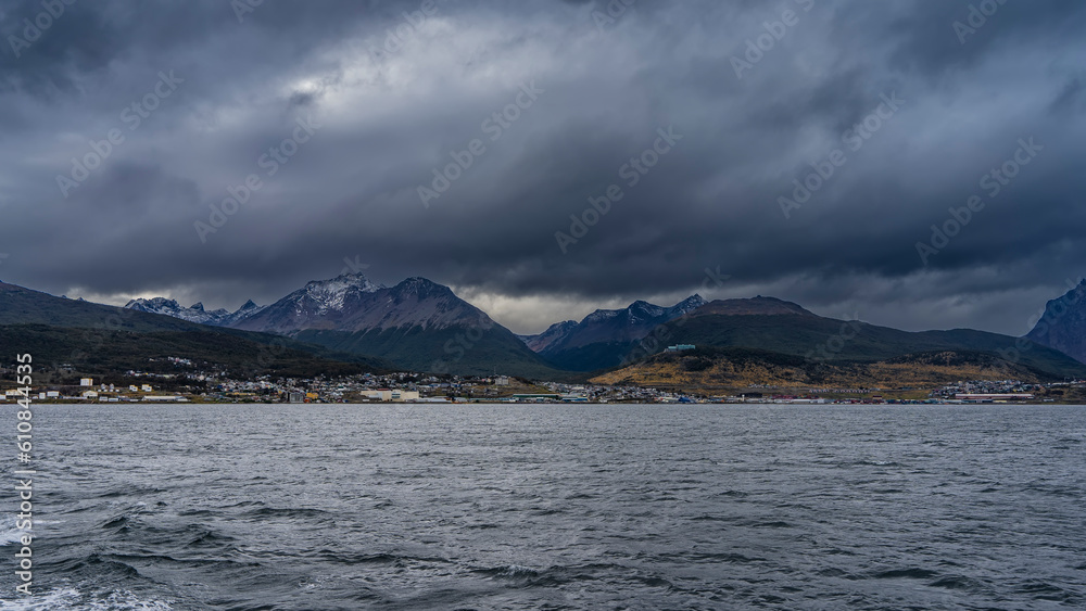 The picturesque Martial mountain range against a cloudy sky. The city houses of Ushuaia are visible on the shore. Ripples on the surface of the Beagle Channel. Argentina. 
