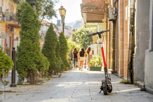 A red electric scooter parked on the sidewalk of the old town against the background of girls leaving on foot