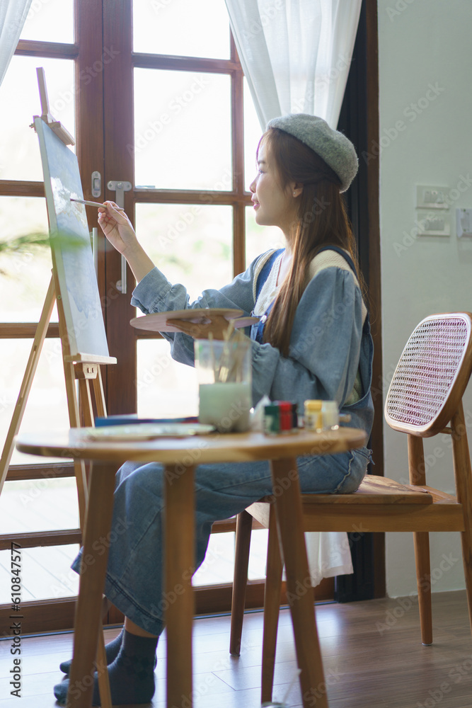 Young female artist using paintbrush to drawing and painting masterpiece on canvas in home studio