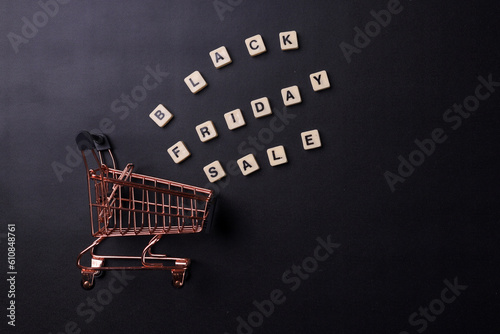 Wooden cubes with the text Black Friday Sale and shopping cart on a black background with copy space. Black Friday Sale and shopping concept