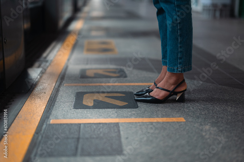 Woman business feet stand in front of arrow sign at train station, Close up Arrow sign on floor at the sky train station, bangkok, Thailand