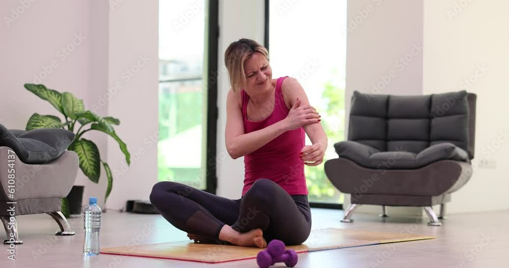Woman touches sore shoulder or arm after workout in living room. Pain exercising at home Woman touches sore shoulder or arm after workout in living room. Pain exercising at home
