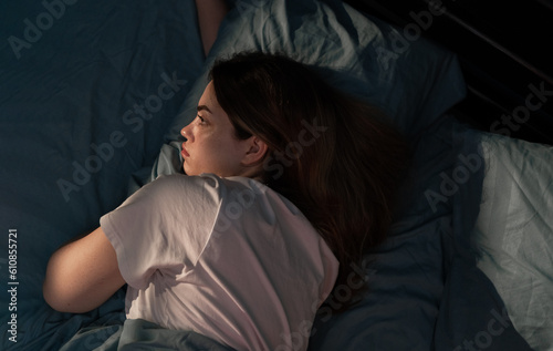 Young sad woman lying in bed late at night trying to sleep suffering insomnia sleeping disorder looking worried. Mental health concept