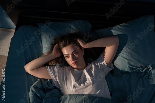 Tapeta Annoyed stressed, young woman suffering from insomnia, awake in bed at night, holding head with hands, disturbed loud noise, unable sleep