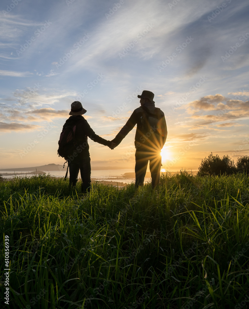 Couple standing on Mt Eden summit and looking at Rangitoto Island at sunrise. Auckland. Vertical format.