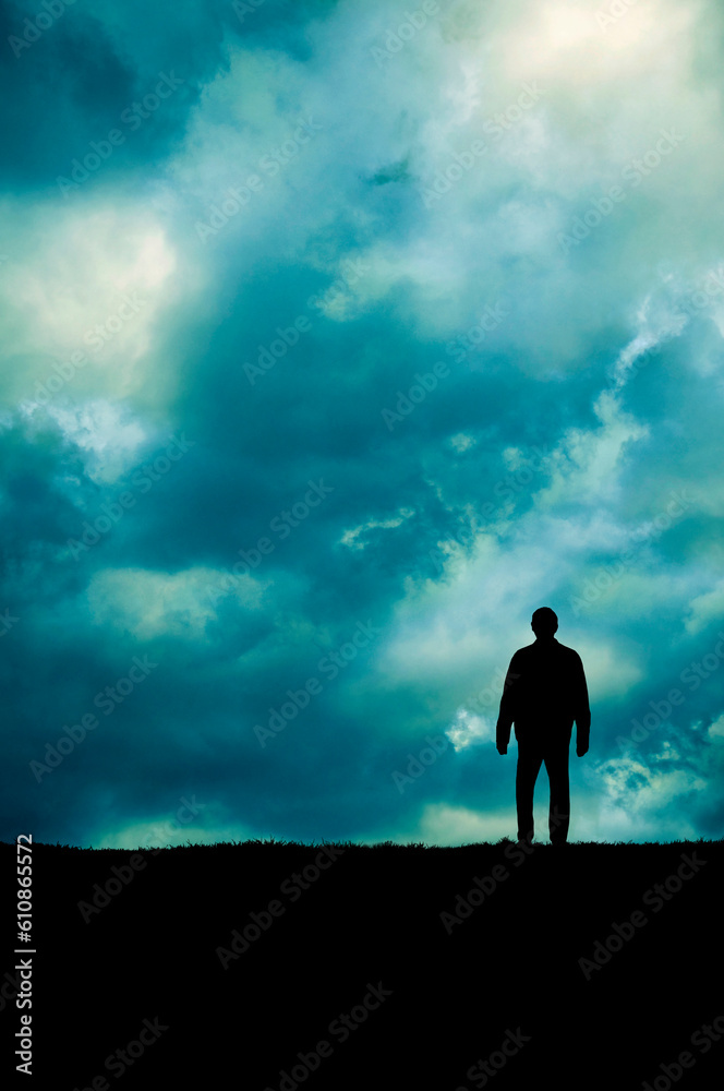 silhouette of a man standing on a meadow with dramatic cloudy sky above