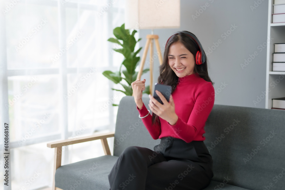 Happy young Asian woman raising hands with victory smiling happily with smart phone at home. Success, win, victory, triumph, congratulation, concept.. Happy young Asian woman raising hands with victory smiling happily with smart phone at home. Success, win, victory, triumph, congratulation, concept..