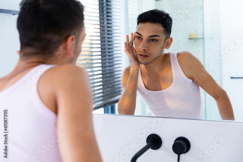 Tableau sur toile Biracial transgender man looking in mirror and touching face in bathroom