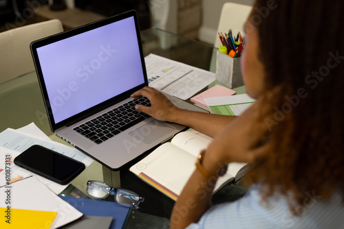 Biracial woman working at home, sitting at dining table using laptop with copy space on screen