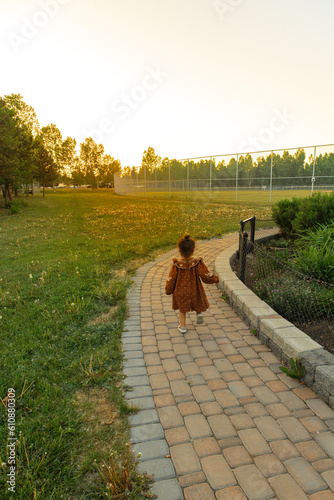 Little toddler in red orange dress running on a brick pathway in green meadows