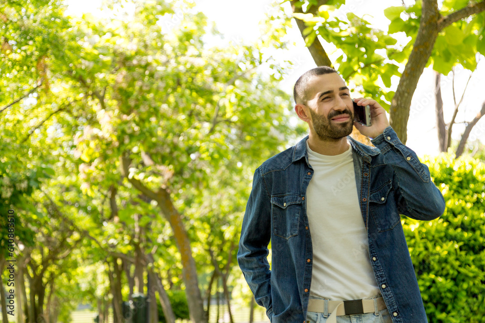 Young bearded man walking among trees, talking on the phone Young bearded man walking among trees, talking on the phone