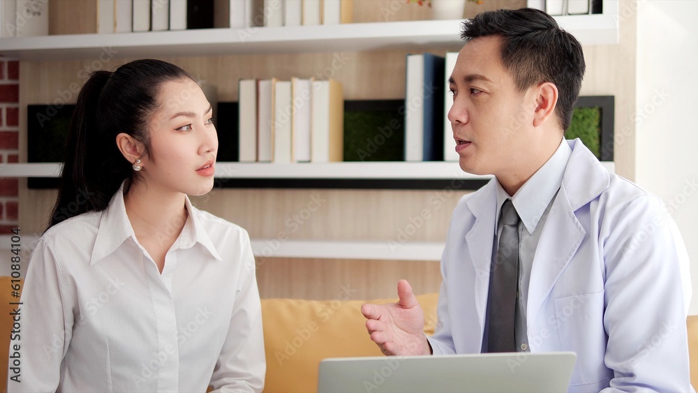 Fototapeta premium Asian doctor man visited patient woman and using laptop to check up health at hospital. Woman patient consulting health problem and symptoms with doctor. Health care service