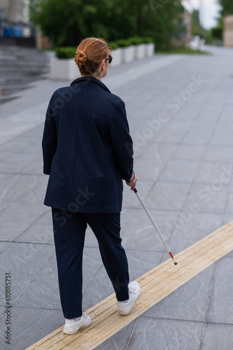 Blind businesswoman walking along tactile tiles with a cane. 