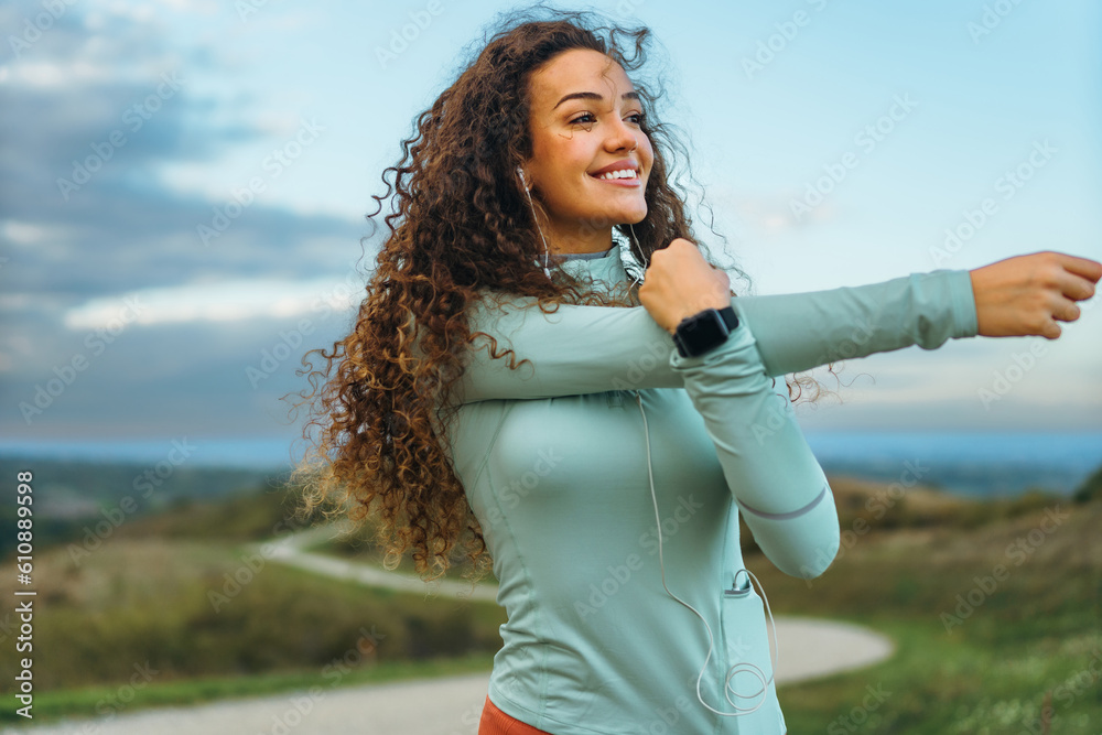 A fitness girl is stretching her arms with an astonishing smile after jogging in nature.