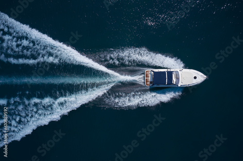 Photo A white large boat with a blue awning is moving fast on dark water, top view