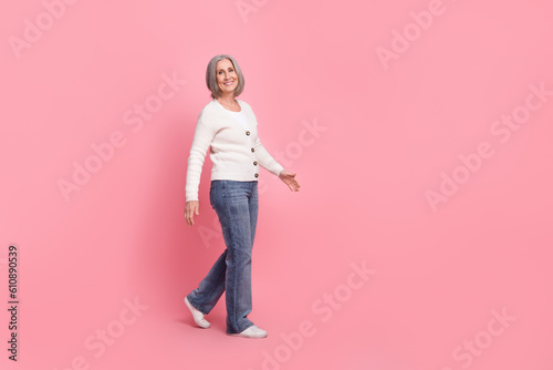 Full body profile photo of cheerful satisfied aged person walking empty space isolated on pink color background
