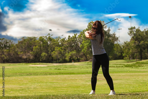 Professional middle aged woman golfer wearing sportswear and sunglasses teeing golf in golf tournament competition. Healthy sports lifestyle and leisure activity concept. Copy advertising text space