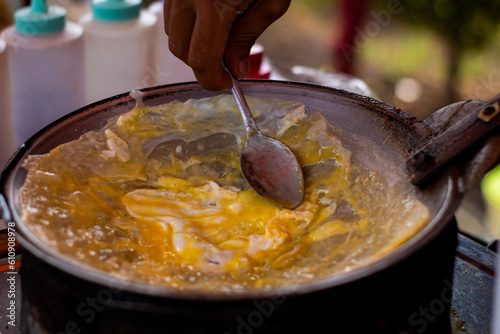 Making papeda at open market festival, eggs cooked on metal griddle stirred with spoon outdoors with food cart. photo