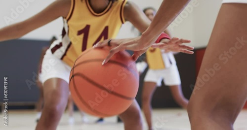 Diverse female basketball team training with male coach in indoor court, in slow motion photo