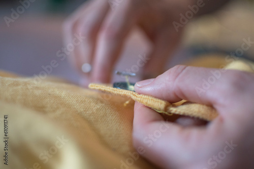 hands sewing on a button of a yellow jacket